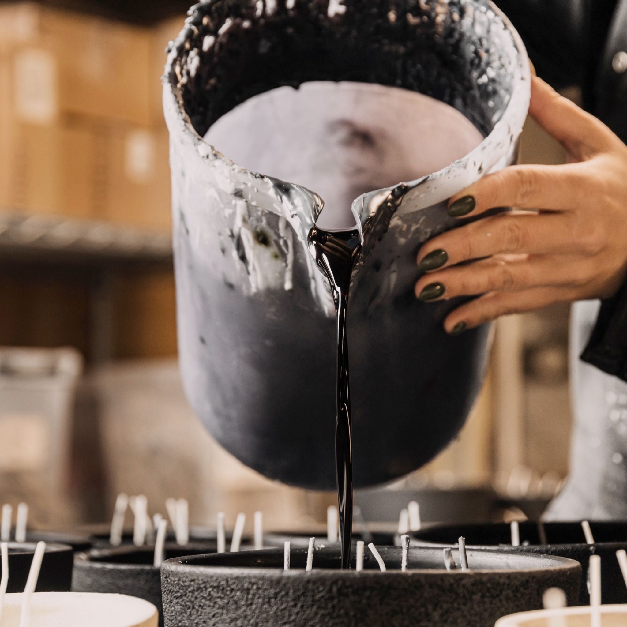 Candle boss pouring black scented wax into a black pot to create a beautiful scented candle.