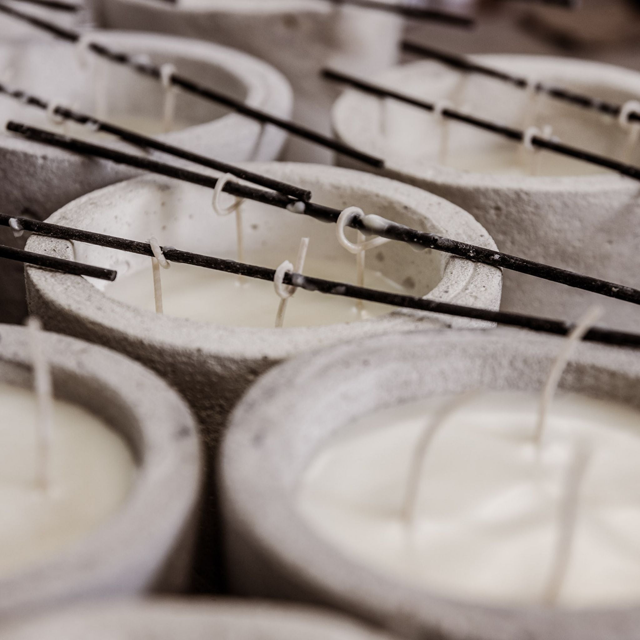 Some candles filled with wax that are drying. The wicks are hold up in the air with little sticks and pegs.