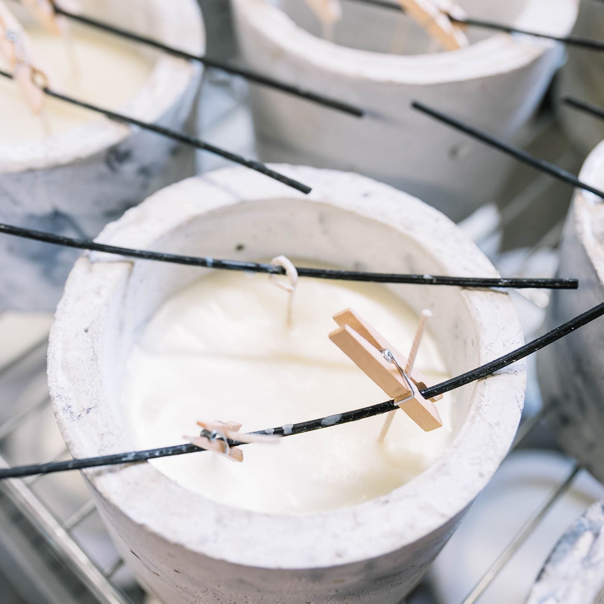 Manufacturing process of handmade candles. Some candles that are drying. The candles are filled with white wax and the wicks are hold up with sticks and pegs.