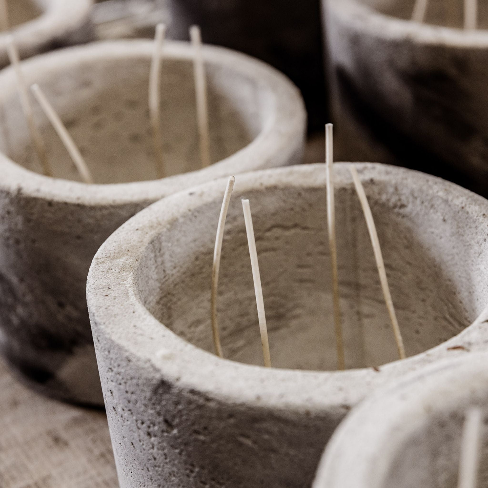 Manufacturing of handmade concrete candles. You see grey concrete pots that will become Mon Dada candles. The wicks are already placed, 4 wicks per candle.