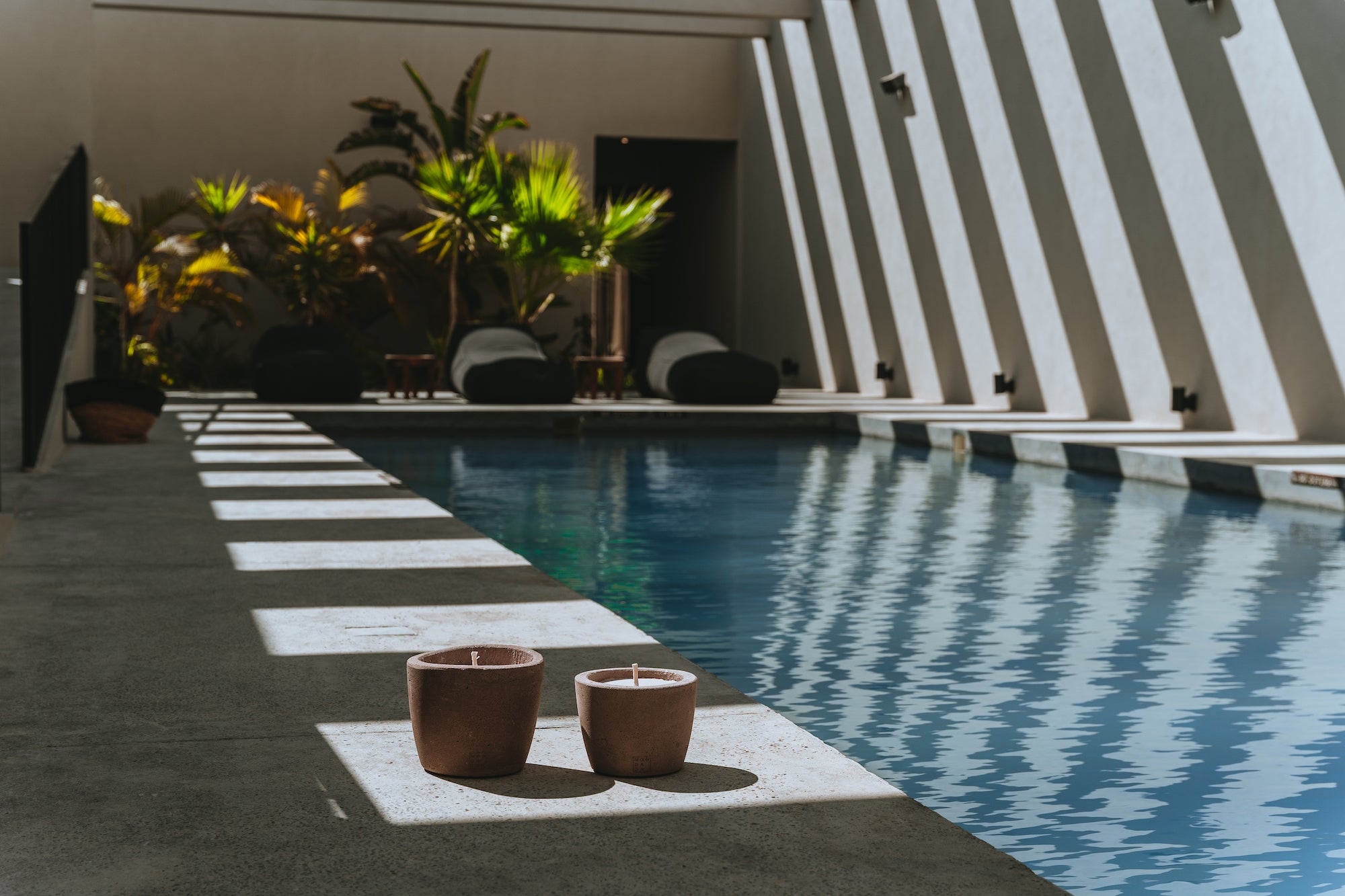 Pool with outdoor candles next to it, tropical plants in the back