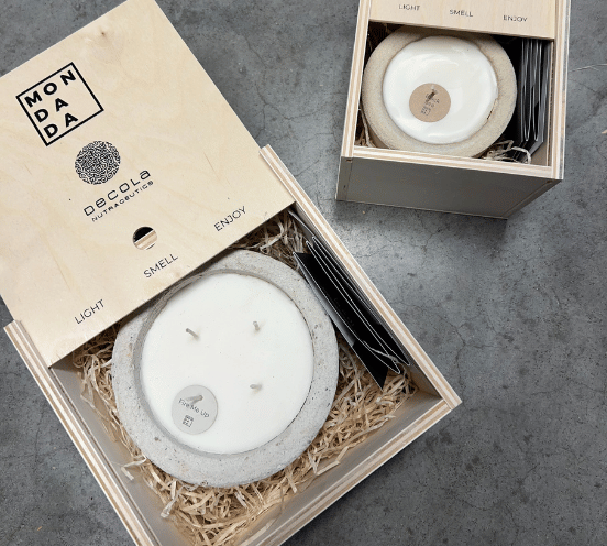 Square wooden corporate gift boxes with Mon Dada logo and personalised logo from the client's company. In the box is a Mon Dada candle in the scent "Fire Me Up", in the colour grey. In the other box in the back is a candle in the colour desert.