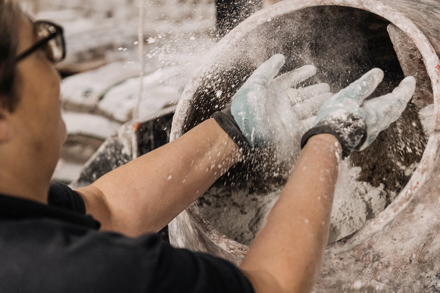 Concrete boss touching sand which she will turn into concrete to manufacture Mon Dada candles. She's wearing gloves for safety.