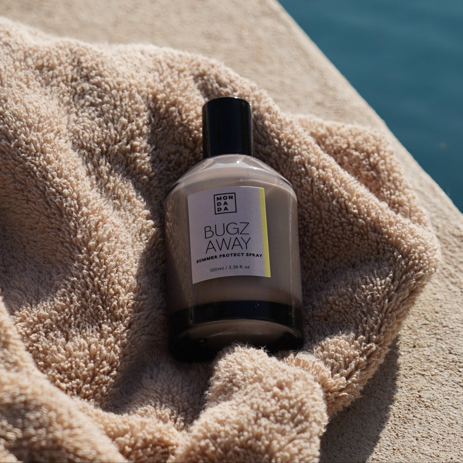 Bottle of mosquito repellent with a towel on a ledge near water
