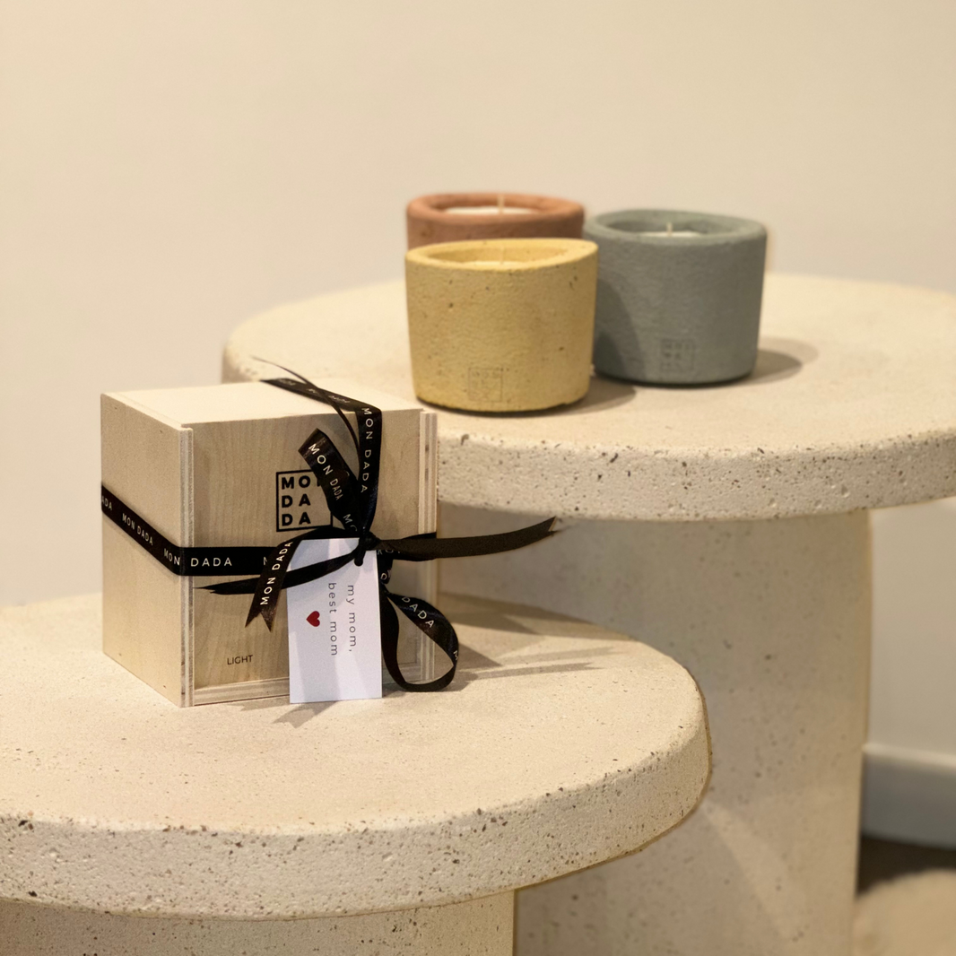 3 concrete candles in 3 colourful colours; mustard, slate and sienna. In front of them is a wooden giftbox with a ribbon and a little card, on which is written " my mom, best mom".