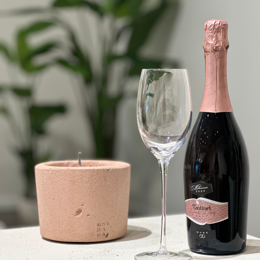 A pink outdoor candle in a pink color and a bottle of prosecco with a glass.